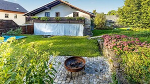 Una casa con porche techado, un hogar de piedra y un jardín bien cuidado con diversas plantas y flores.