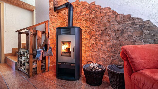 Una estufa de leña con un fondo de pared de piedra, un banco de madera y una silla roja.