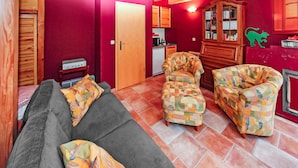 Un salon chaleureux avec un canapé et deux fauteuils, un meuble en bois et, au fond, un coin cuisine.