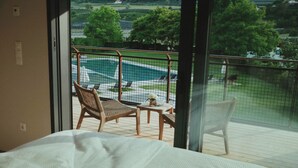 Et soveværelse med balkonudsigt over en swimmingpool og grønt område.