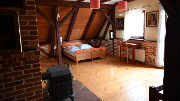Une chambre confortable située sous les toits, avec des poutres apparentes, un lit en bois, une petite table et une cheminée.