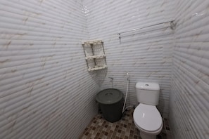 A small, tiled bathroom with a toilet, a trash bin, and a shelf. - OYO 93814 Amanda Homestay (Bandar Lampung)