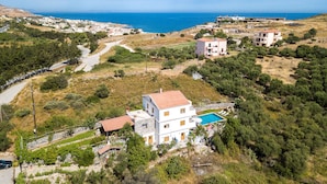 A multi-story building with a swimming pool, surrounded by trees and a view of the sea.