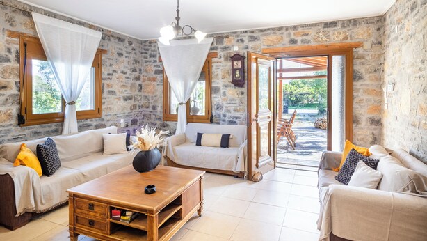 A spacious living room with a stone wall, wooden furniture, and a view to the outside.