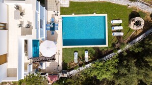 An aerial view of a modern house with a swimming pool, outdoor seating, and a stone pathway.