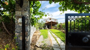 A stone wall with a metal gate leading to a house with a garden.