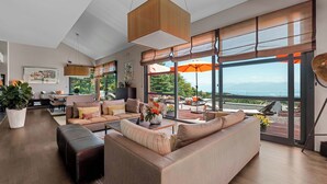 Un salón amplio con un sofá grande, una mesa de centro y vistas al exterior a través de amplios ventanales.