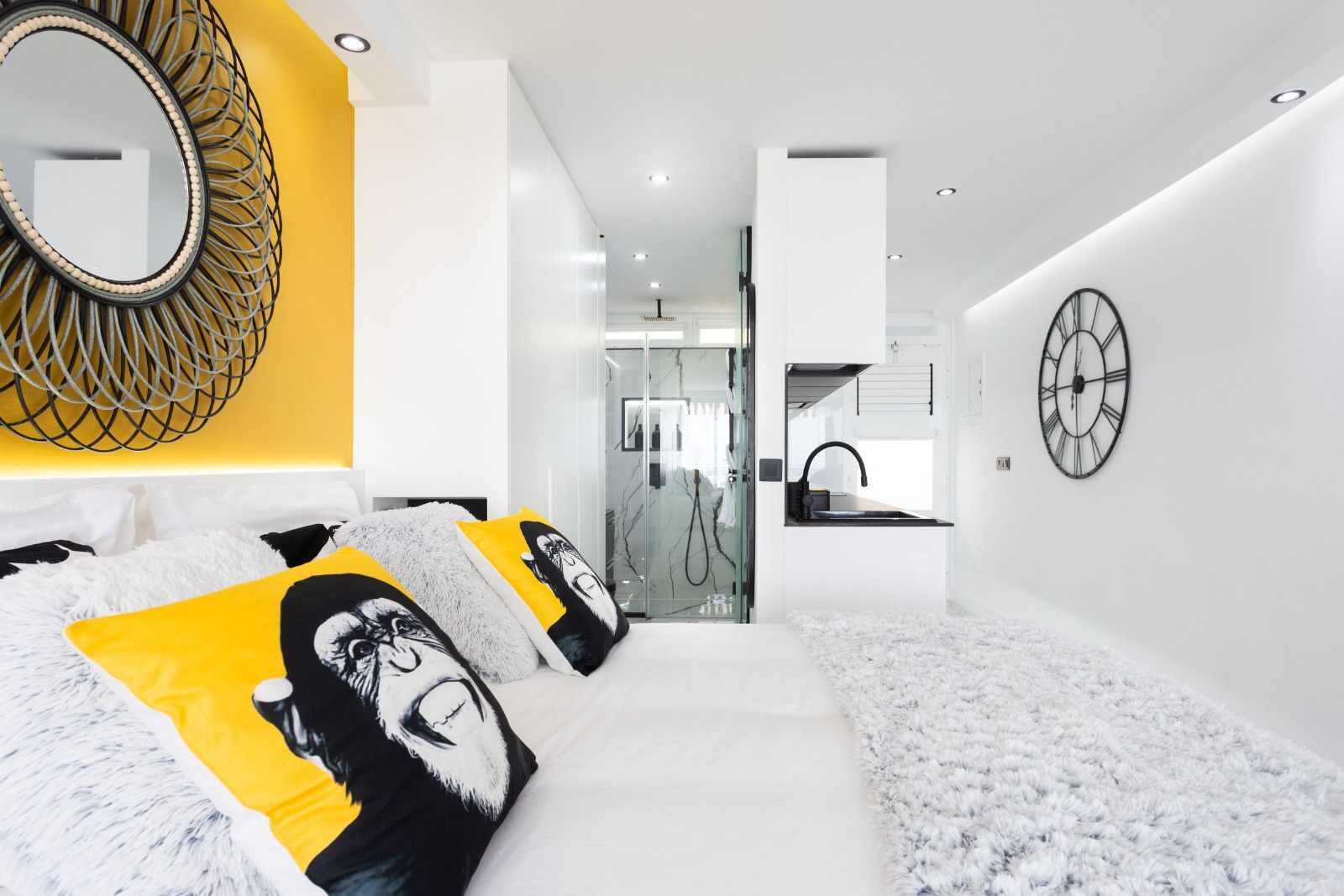 Quarto moderno com cama, espelho e relógio na parede.