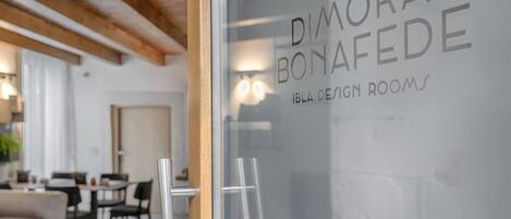 A modern interior with a glass door displaying the name "DIMORA BONAFEDE" and "IBLA DESIGN ROOMS".