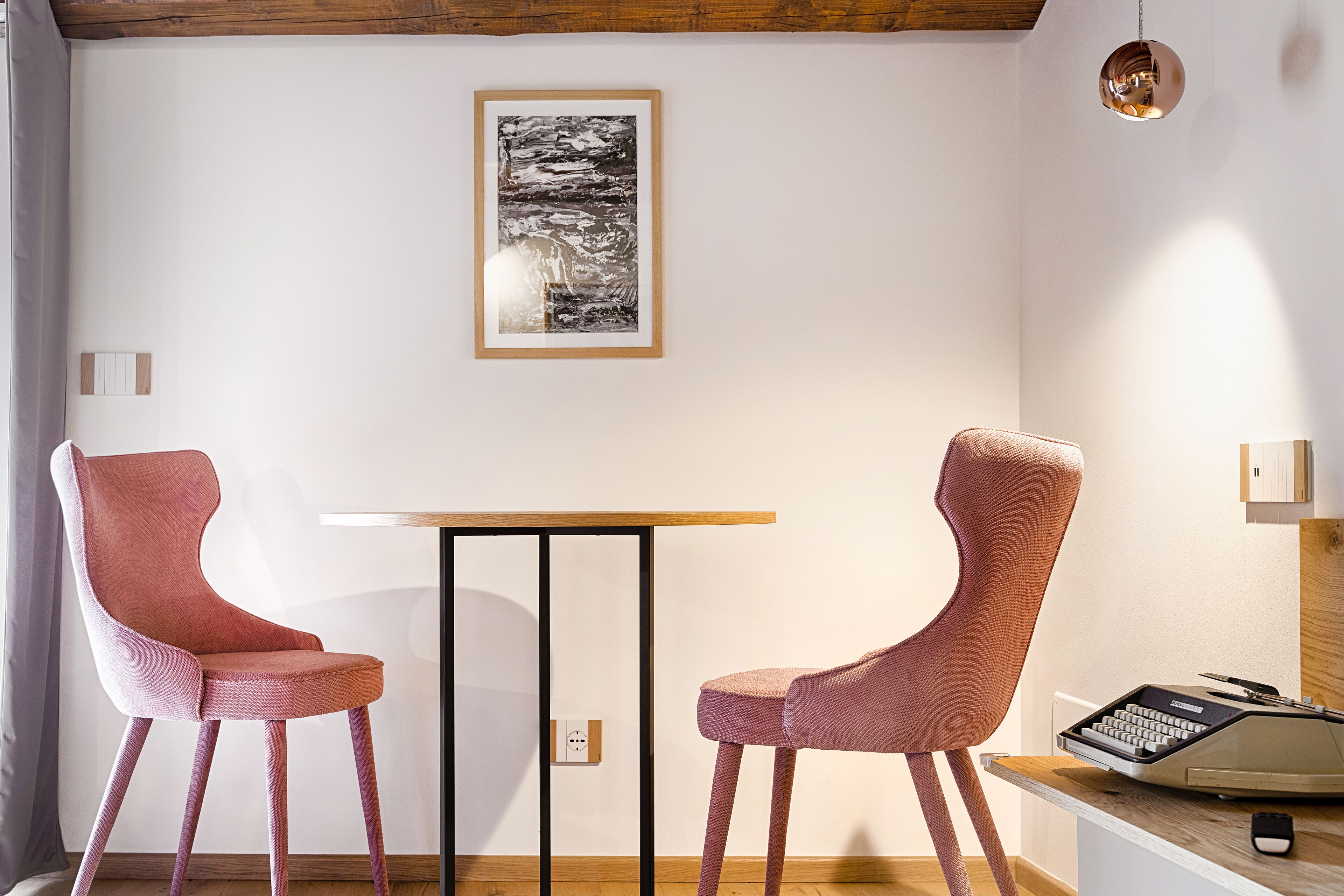A room with two pink chairs, a small table, a vintage typewriter, and a framed picture on the wall.