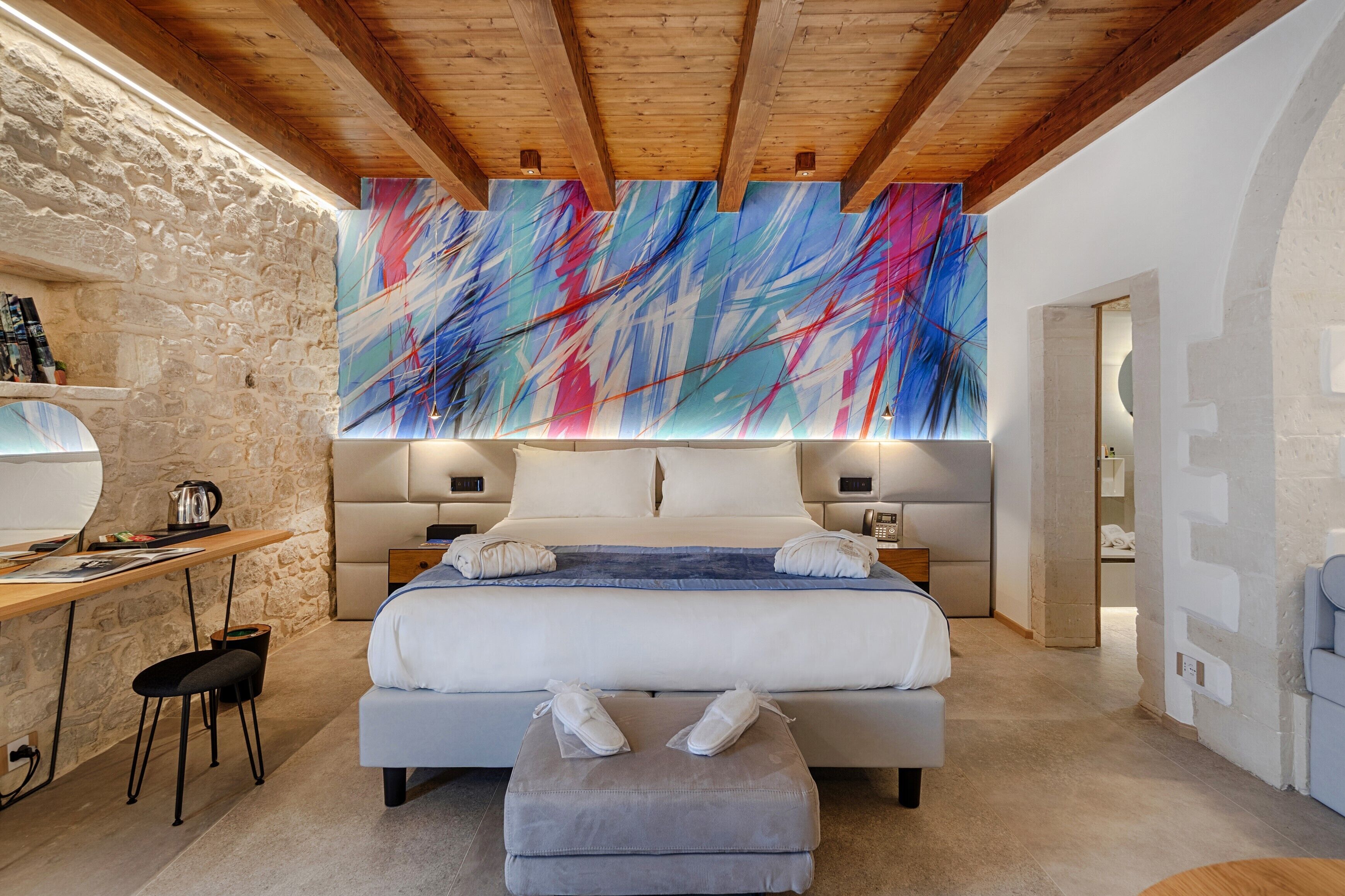 Un dormitorio moderno con una cama grande, un escritorio y una pared de piedra.