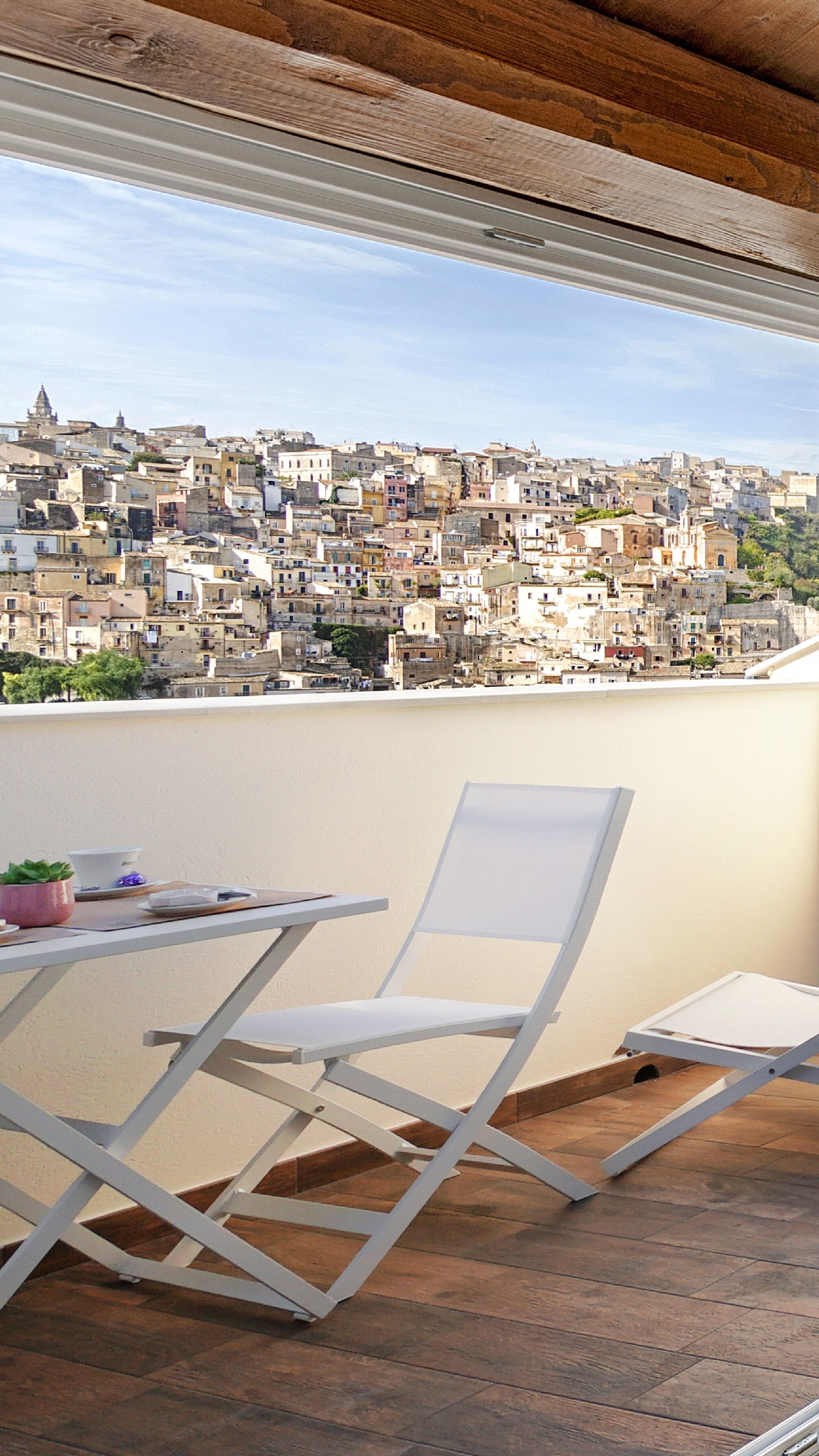 A balcony with a white chair and table, overlooking a densely packed urban area with historic buildings.