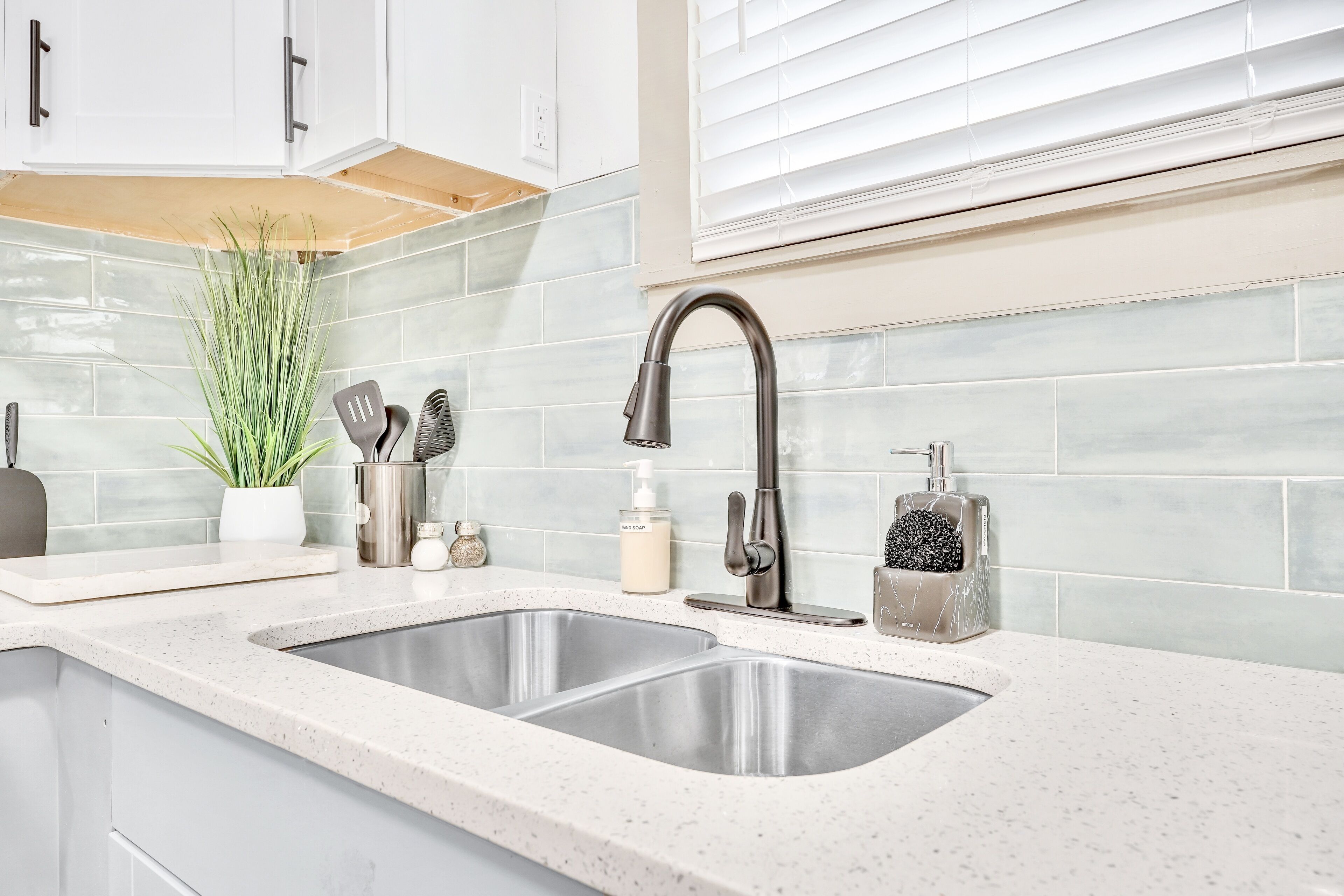 A kitchen with two stainless steel sinks, a modern faucet, and a backsplash of light-colored tiles.
