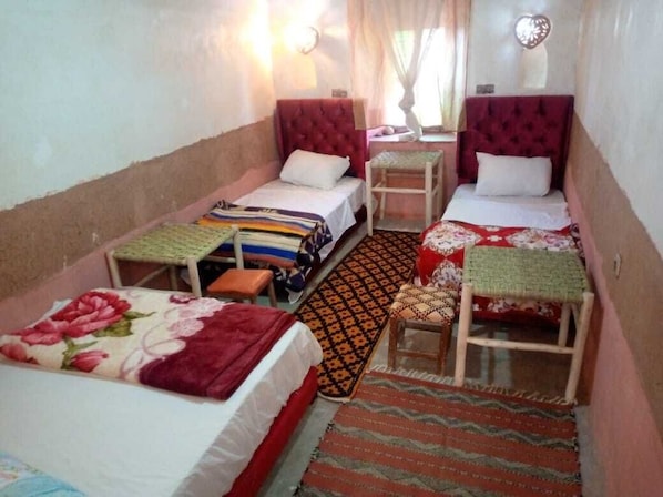 A narrow room with two beds, a small table, and a bench.