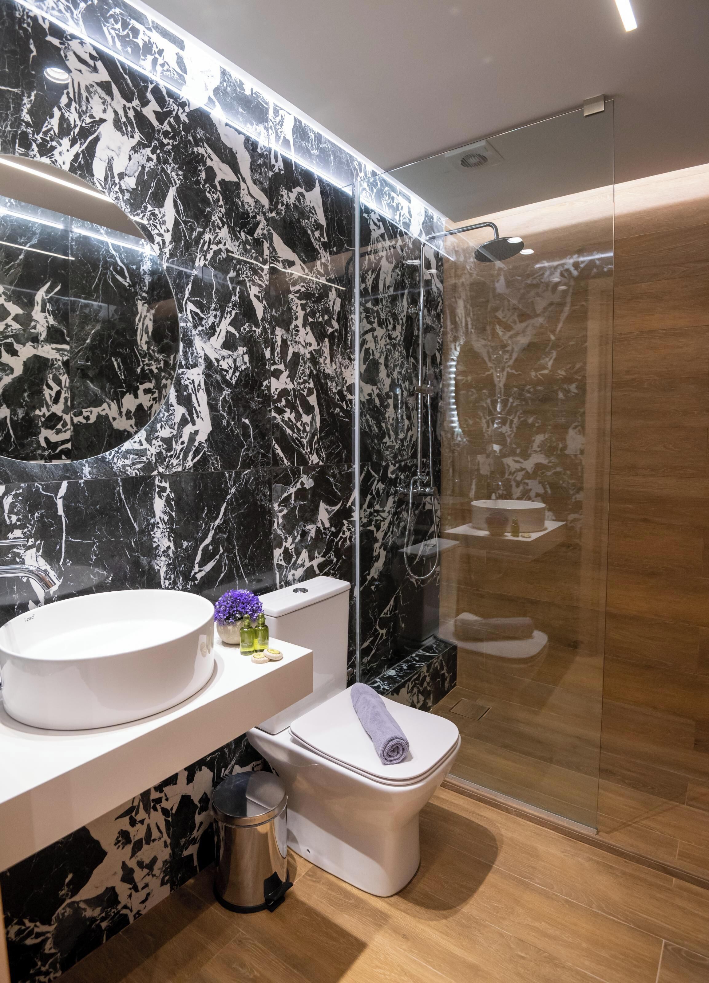 A modern bathroom with a marble backsplash, a white sink, and a glass-enclosed shower.