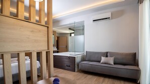 Una sala de estar moderna con un sofá, una mesa redonda de madera con un florero, un separador de vidrio y un muro espejado.