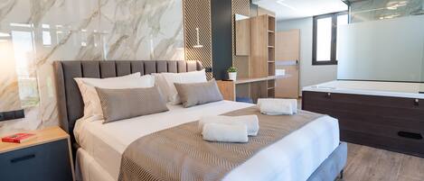 Une chambre d’hôtel moderne avec un mur en marbre, un grand lit doté d’une tête de lit en bois, une table de chevet avec un livre et un grand miroir.