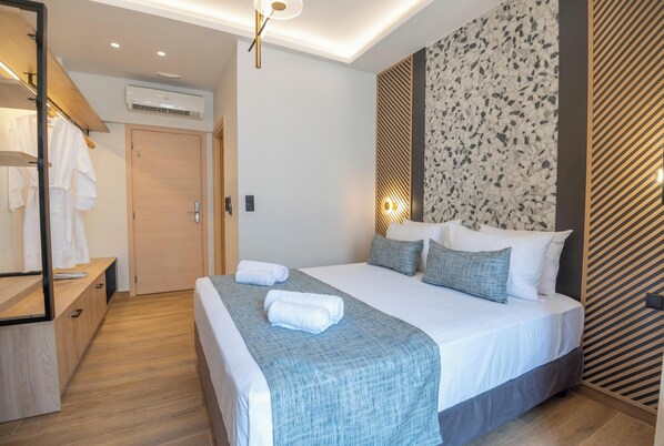 A modern hotel room with a large bed, a wooden wardrobe, and a mirror. - John Mary Suites (Rethymno)