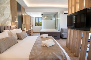 A modern hotel room with a large bed, a TV, a shower area, and a wooden accent wall. - John Mary Suites (Rethymno)