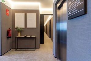 A hallway with a fire extinguisher, a potted plant, and a sign indicating a fitness zone, laundry zone, and restroom. - Feelathome Nervión Apartments (Seville)
