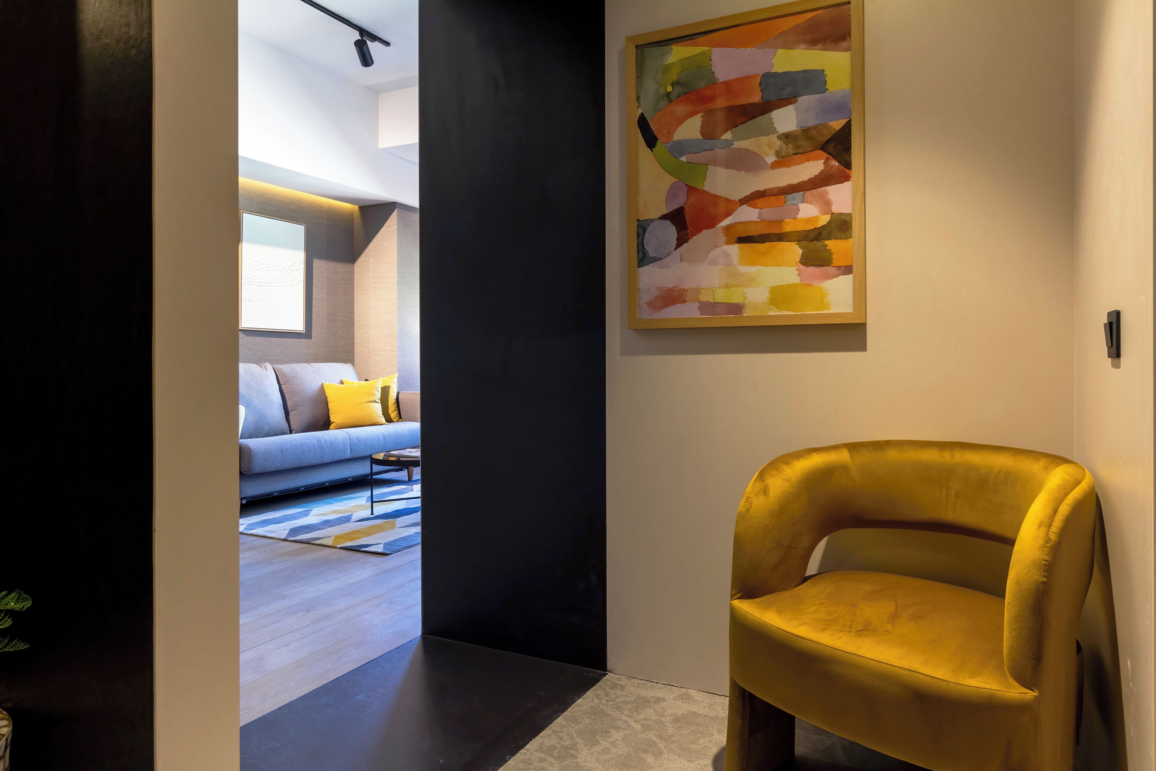Um interior moderno com uma poltrona amarela, uma pintura abstrata colorida e uma sala de estar com sofá e almofadas.