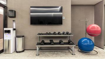 Ein Fitnessbereich mit Kurzhanteln, Wasserspender, Mülleimer, Fernseher und Gymbällen.