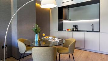 Een moderne keuken met een glazen eettafel, twee stoelen, een vaas met bloemen en een koffiezetapparaat.