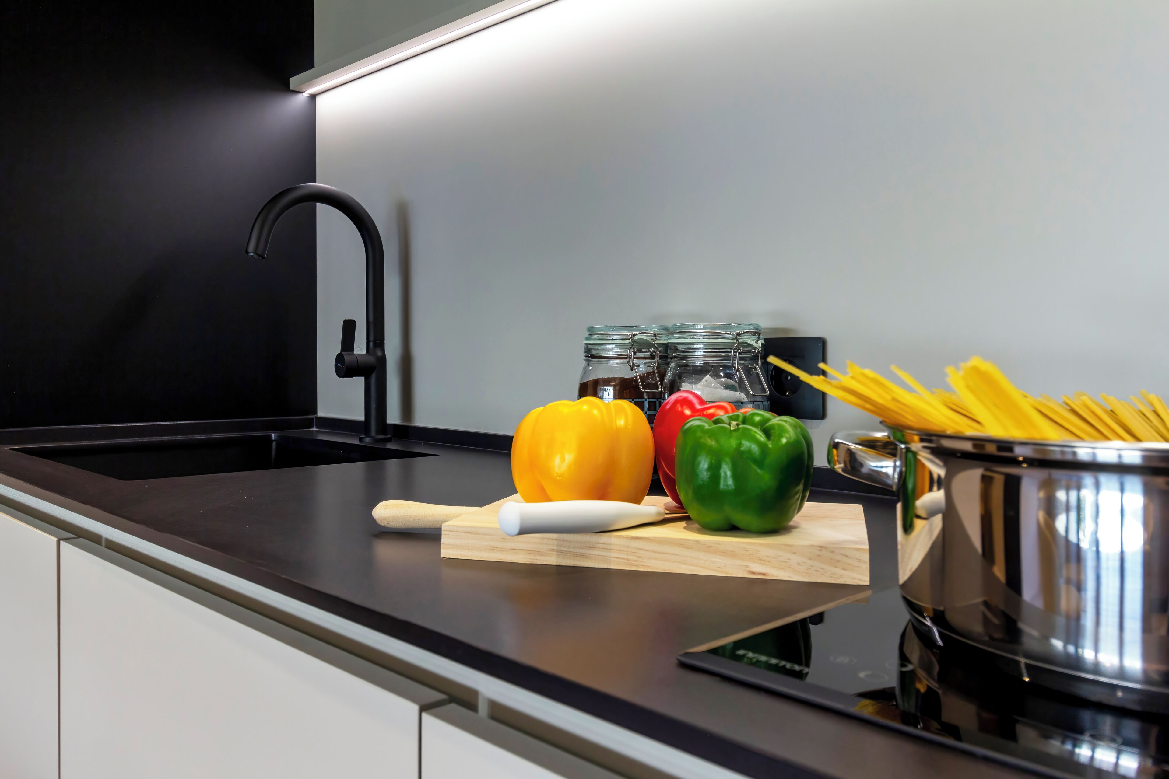 A kitchen counter with a sink, a cutting board with vegetables, a rolling pin, and a pot of spaghetti.
