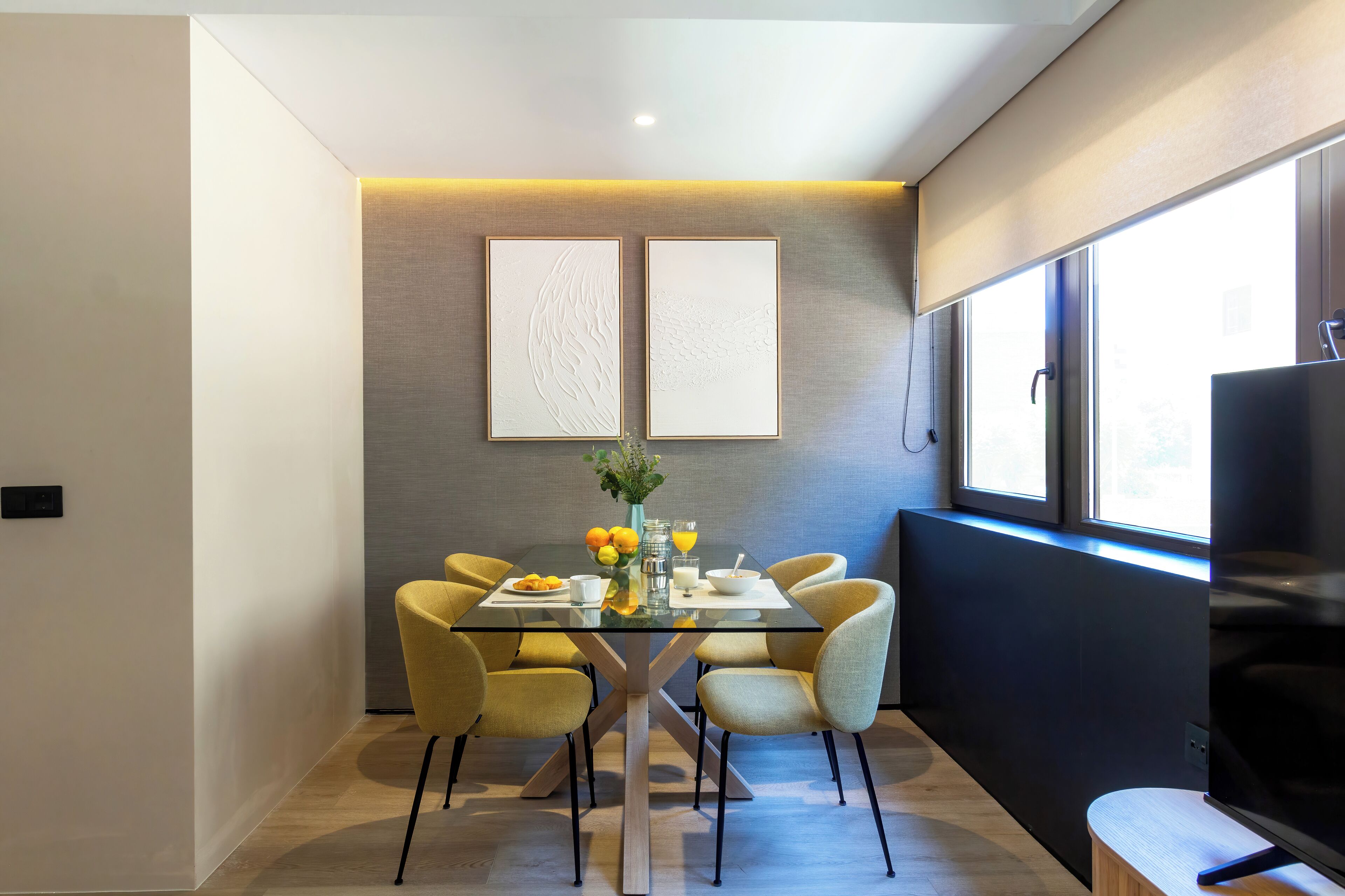 Un espace repas moderne avec une table en verre, des chaises jaunes et un vase rempli de fleurs.