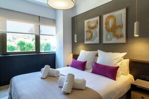 A modern hotel room with a large bed, white and purple pillows, and neatly folded towels. - Feelathome Nervión Apartments (Seville)