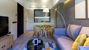 A modern living room with a sofa, coffee table, and a dining area with chairs and a table. - Feelathome Nervión Apartments (Seville)