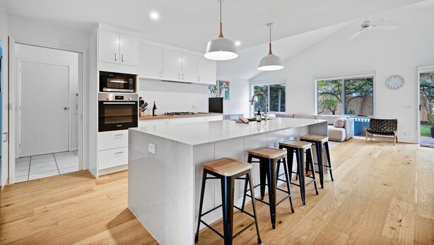 Une cuisine moderne avec des meubles blancs, un grand îlot central doté de tabourets et un éclairage suspendu.