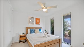 Une chambre avec un lit en bois, un ventilateur de plafond, une table de chevet avec une lampe et une fenêtre donnant sur un paysage verdoyant.