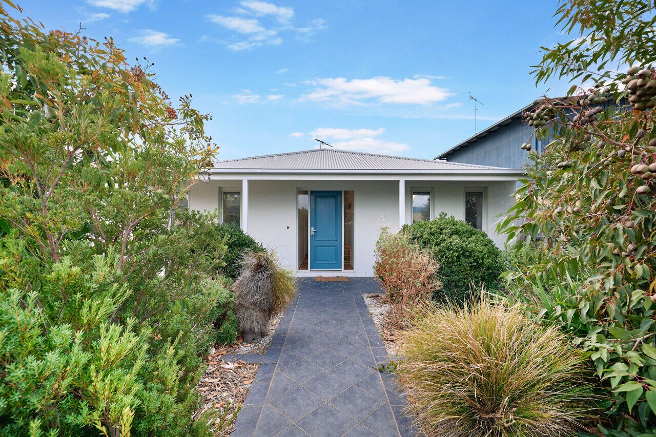 A modern house with a blue door, surrounded by lush greenery and a paved pathway leading to the entrance.