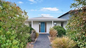 Une maison moderne avec une porte bleue, entourée d’une végétation luxuriante et un chemin pavé menant à l’entrée.