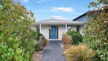A modern house with a blue door, surrounded by lush greenery and a paved pathway leading to the entrance.