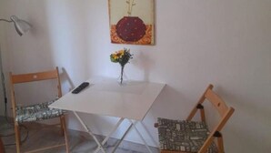 A small dining area with a white table, two patterned chairs, a vase with flowers, and a wall-mounted lamp. - Comeacasa. (Salerno)