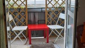 A balcony with a red table and two white chairs, a grey sofa, and a wooden lattice partition. - Comeacasa. (Salerno)