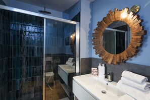Un baño moderno con ducha envuelta en vidrio, un espejo grande con marco de madera y un lavamanos blanco con toallas.