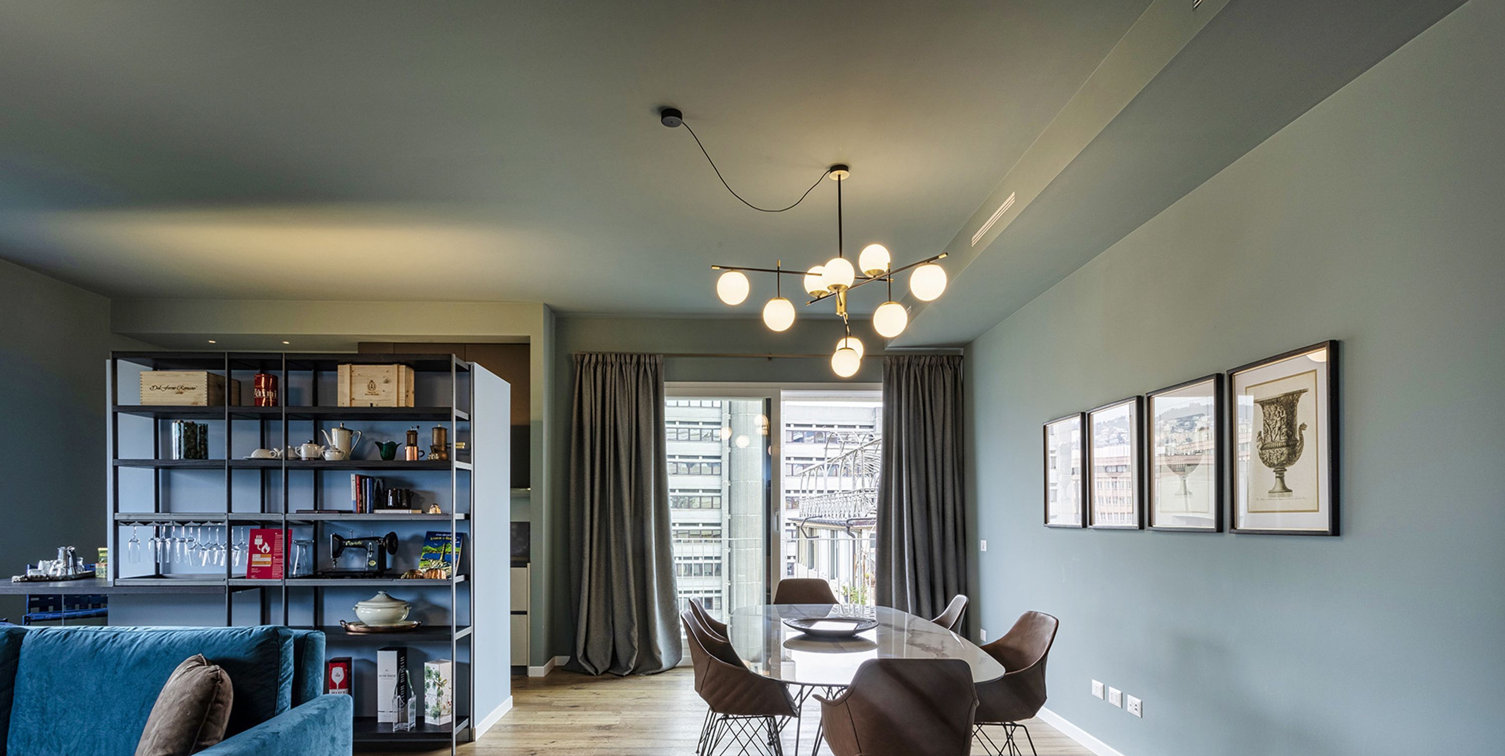 A modern living room with a blue sofa, a glass dining table, and a bookshelf filled with books and decorative items.