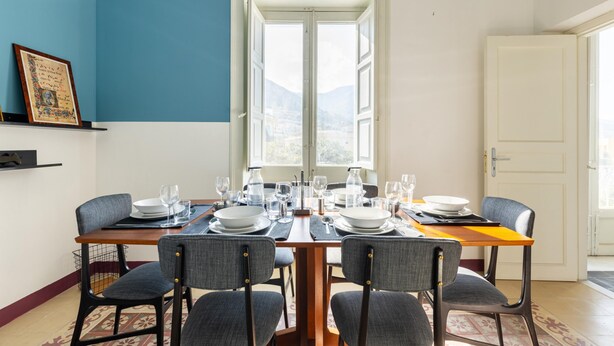 A dining area with a table set for four, chairs, and a window with a view of mountains. - Charming House in Cefal by Wonderful Italy (Cefalù)