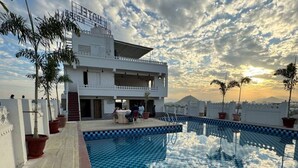 A rooftop pool with a checkered pattern, surrounded by potted plants and a white building with balconies. - Hotel Rudrakripa (Udaipur)