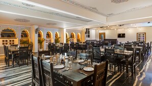 A spacious dining area with multiple tables and chairs, decorative ceiling patterns, and a modern chandelier. - Hotel Rudrakripa (Udaipur)
