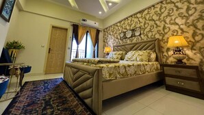 A bedroom with a bed, bedside tables, a nightstand, a patterned wall, and a ceiling with recessed lighting. - the Realtors inn Luxurious 1bed Apartment dha 2 (Islamabad)