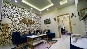 A modern living room with a patterned wall, a blue sofa, a coffee table, and a television. - the Realtors inn Luxurious 1bed Apartment dha 2 (Islamabad)