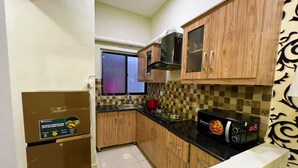 A compact kitchen with wooden cabinets, a microwave, a stove, and a refrigerator. - the Realtors inn Luxurious 1bed Apartment dha 2 (Islamabad)