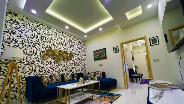 A modern living room with a patterned wall, a blue sofa, a coffee table, and a colorful rug. - the Realtors inn Luxurious 1bed Apartment dha 2 (Islamabad)