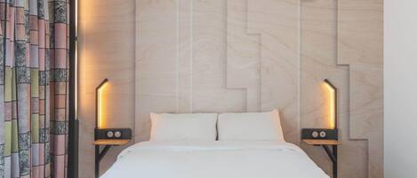 A hotel room with a bed, two bedside tables, a patterned curtain, and a wall with a geometric design.