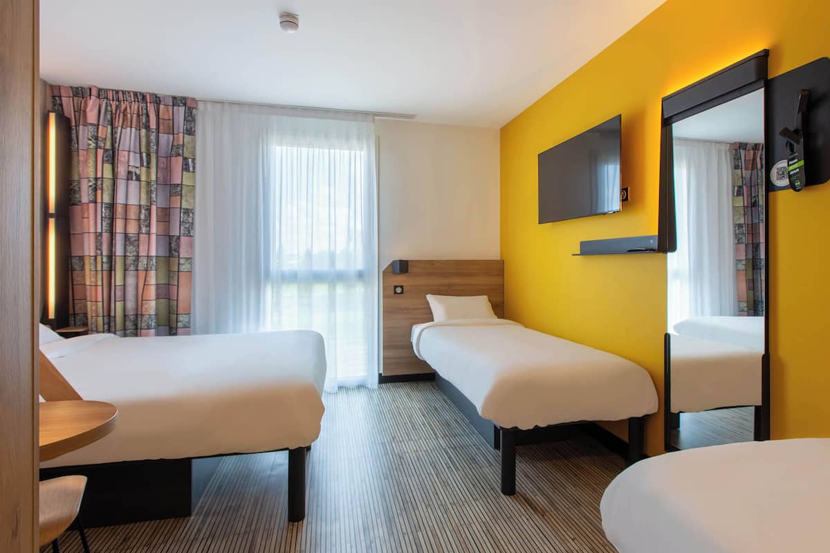 A hotel room with two beds, a TV, a mirror, and a desk.
