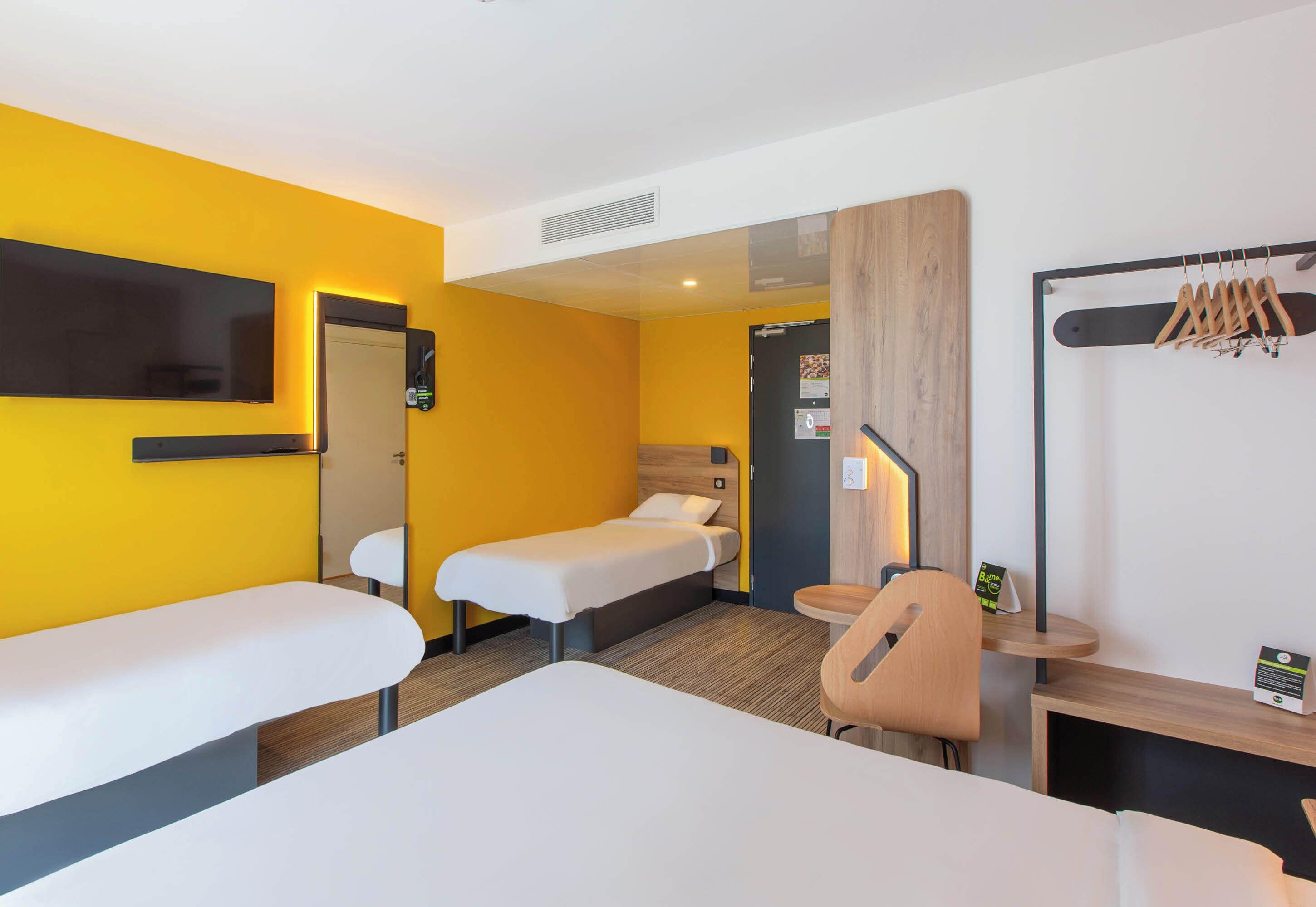 Una habitación de hotel con dos camas, una zona de estar, un televisor y un perchero.